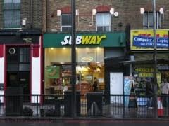 Exterior of a Subway shopfront viewed through glass, seating visible inside.